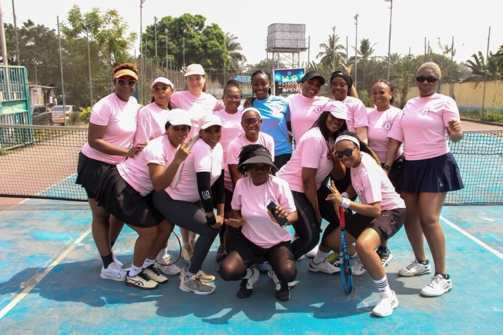 Players and volunteers in pink tournament shirts posing together courtside